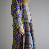 Rieti Striped Kimono in Grey, shown reversible with woven grey striped fabric on one side and a purple-green geometric print on the other, worn open with a tie belt against a plain grey background.