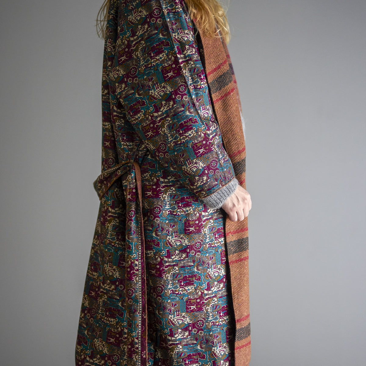 Rieti Kimono in Brown, reversible wrap shown with patterned side worn outward, striped brown lining peeking at cuffs and lapel, tied belt at waist, against a plain grey background.