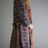 Rieti Kimono in Brown, reversible wrap shown with patterned side worn outward, striped brown lining peeking at cuffs and lapel, tied belt at waist, against a plain grey background.
