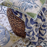 Santena Wavy Cotton Throw in blue with a woven wave and dot pattern, draped over a woven basket beside floral cushions on patterned tile flooring.