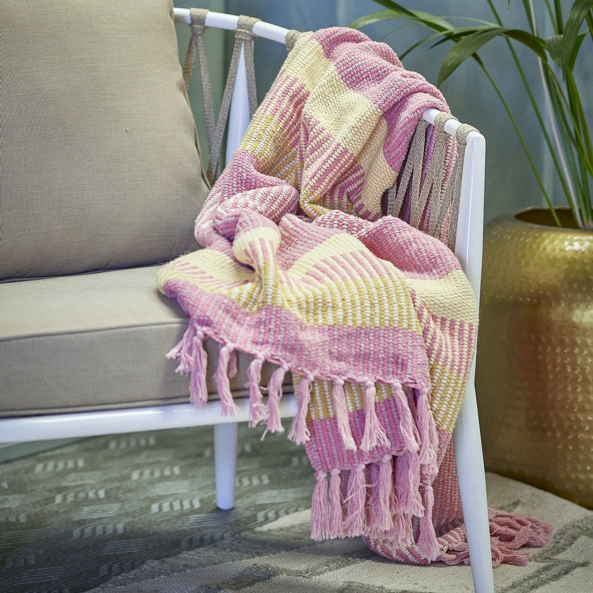 Isnel Striped Throw in Pink and yellow woven fabric with knotted tassel fringe, draped over a white armchair in a living room setting.