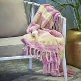 Isnel Striped Throw in Pink and yellow woven fabric with knotted tassel fringe, draped over a white armchair in a living room setting.