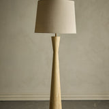Leonor Wooden Floor Lamp with a natural rubberwood column, narrow waist and tapered linen drum shade, shown against a plain neutral background.