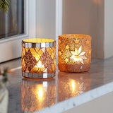 Miya Round Glass Christmas Tealight Holders Set of 2 in Nude, lit on a marble windowsill, one with a diamond mosaic and mirrored bands, the other with a star mosaic design.