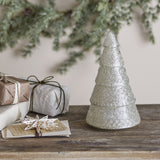 Emilius glass Christmas tree decoration in white, tiered fir shape with textured surface, displayed on a wooden surface beside wrapped gifts and greenery.