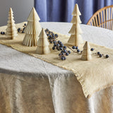 Milan Paper Christmas Decorations Set of 5 in cream, five tiered folded-paper trees of varying heights styled on a table runner with dark berries, a pale tablecloth and blue curtain behind.