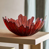 Aila Glass Bowl 31cm in Copper, a ridged glass decorative bowl with an irregular wavy rim, shown on a wooden side table in a living room setting.