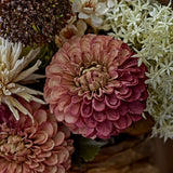 Artificial chrysanthemum stem with a full, rounded pink flower head in layered cupped petals, shown close-up among other dried-style blooms in warm pink and cream tones.