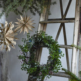 Cedar Artificial Christmas Wreath, 50x11cm, green faux cedar ring with pinecones and frosted tips, shown hanging near paper stars and a wooden ladder.