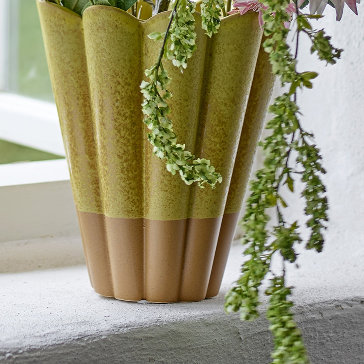 Penn Speckled Stoneware Vase in yellow, fluted scalloped rim with a speckled glaze fading to an unglazed terracotta base, shown on a windowsill with trailing foliage.