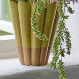 Penn Speckled Stoneware Vase in yellow, fluted scalloped rim with a speckled glaze fading to an unglazed terracotta base, shown on a windowsill with trailing foliage.
