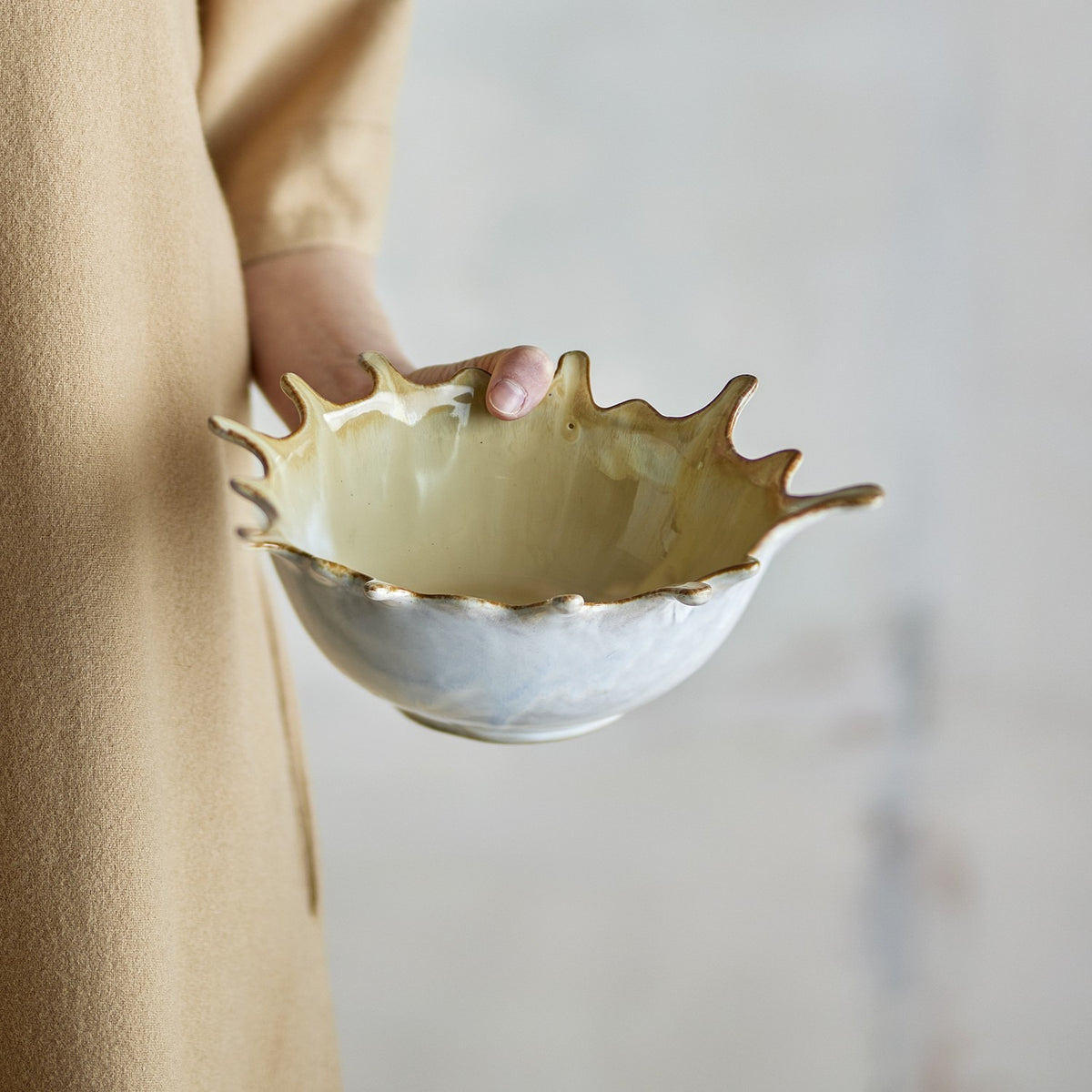 Hand holding the Alcott Stoneware Bowl 24x21cm in beige, featuring a splash-like rim with pointed edges and a white glazed base.