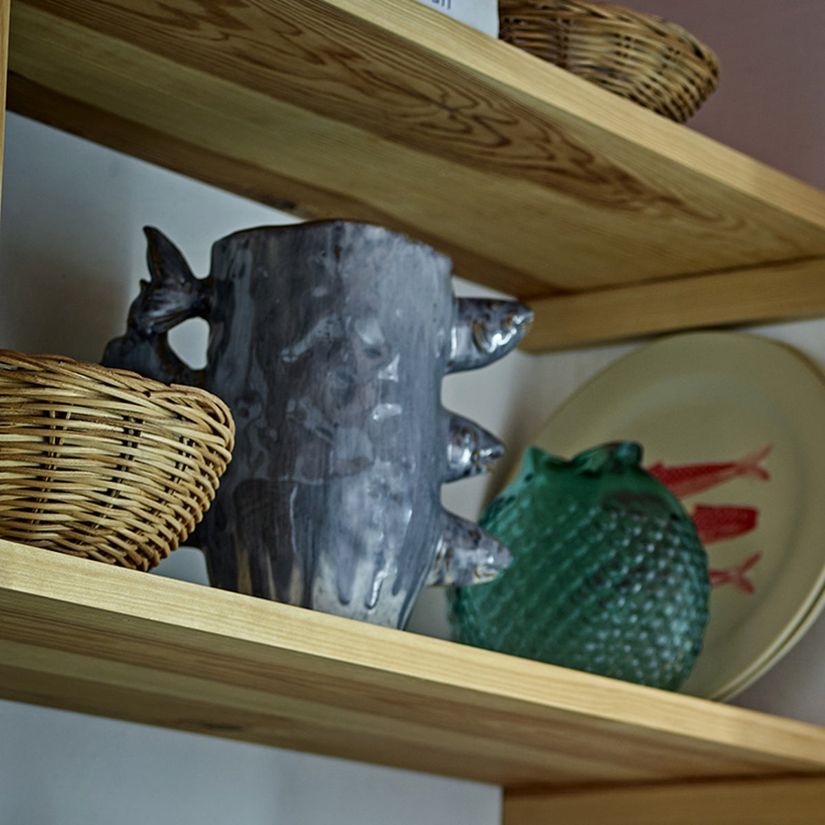 Tace Stoneware Vase 23cm in blue with sculpted fish heads and tails, shown on a wooden shelf beside woven baskets and a green decorative piece.