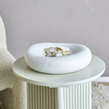 Audra Pebble Stoneware Bowl 30cm in White, a round pebble-shaped dish with a speckled finish holding seashells, displayed on a ridged pedestal side table.