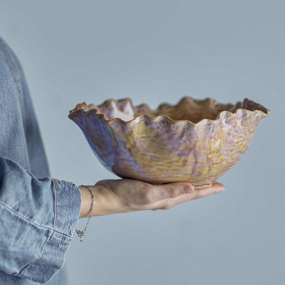 Nash Stoneware Bowl 24.5cm in Brown held in one hand, showing its ruffled wavy rim and rippled ceramic texture against a plain grey background.