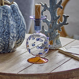 Phila Glass Candle Holder in Blue, a clear puffer fish-shaped glass candle holder with blue spine dots and a flared cup, holding a candle on a wooden table.