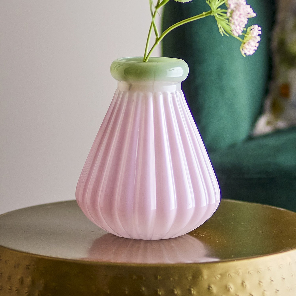 Judith Fluted Glass Vase 20cm in pink with a green rolled rim and ribbed body, holding a flower stem on a gold tray against a dark green backdrop.