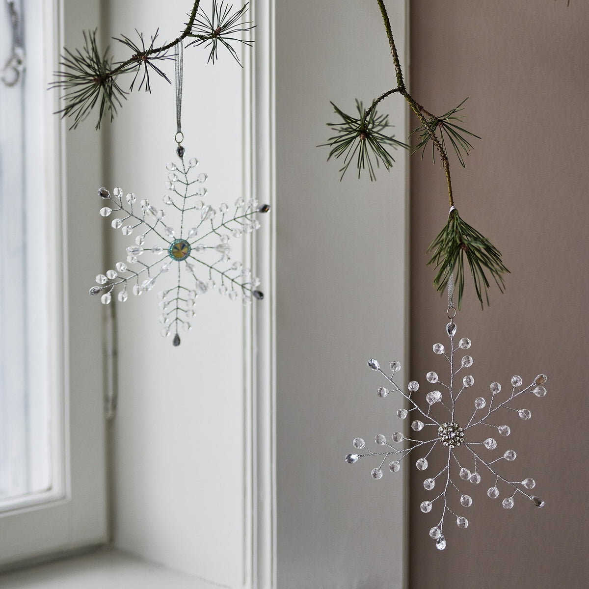Miku Snowflake Christmas Tree Decorations, set of 2 clear beaded wire snowflakes, hanging from pine branches with one faceted centrepiece and one beaded cluster centre.