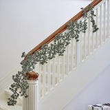 Artificial cedar Christmas garland in frosted green draped along a white staircase handrail with wooden rail cap and turned newel post.