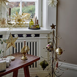 Wen Iron Christmas Decoration in gold, a slim-stemmed tabletop tree with curved tiered arms and hooks topped by a star, styled with baubles on a wooden bench in a living room.