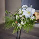 Kristin Artificial Christmas Bouquet in White, with large trumpet-shaped blooms, pine needles, frosted leaves and white berry clusters, displayed on a chair indoors.