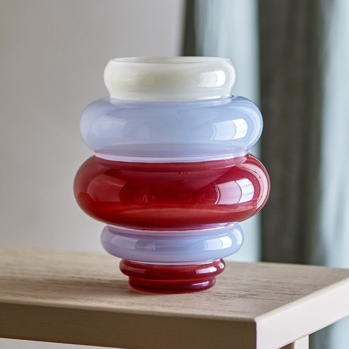 Annhelene Glass Vase 24cm in Multi, with stacked rounded tiers in white, periwinkle blue, and red glass, shown on a wooden table against a muted interior backdrop.