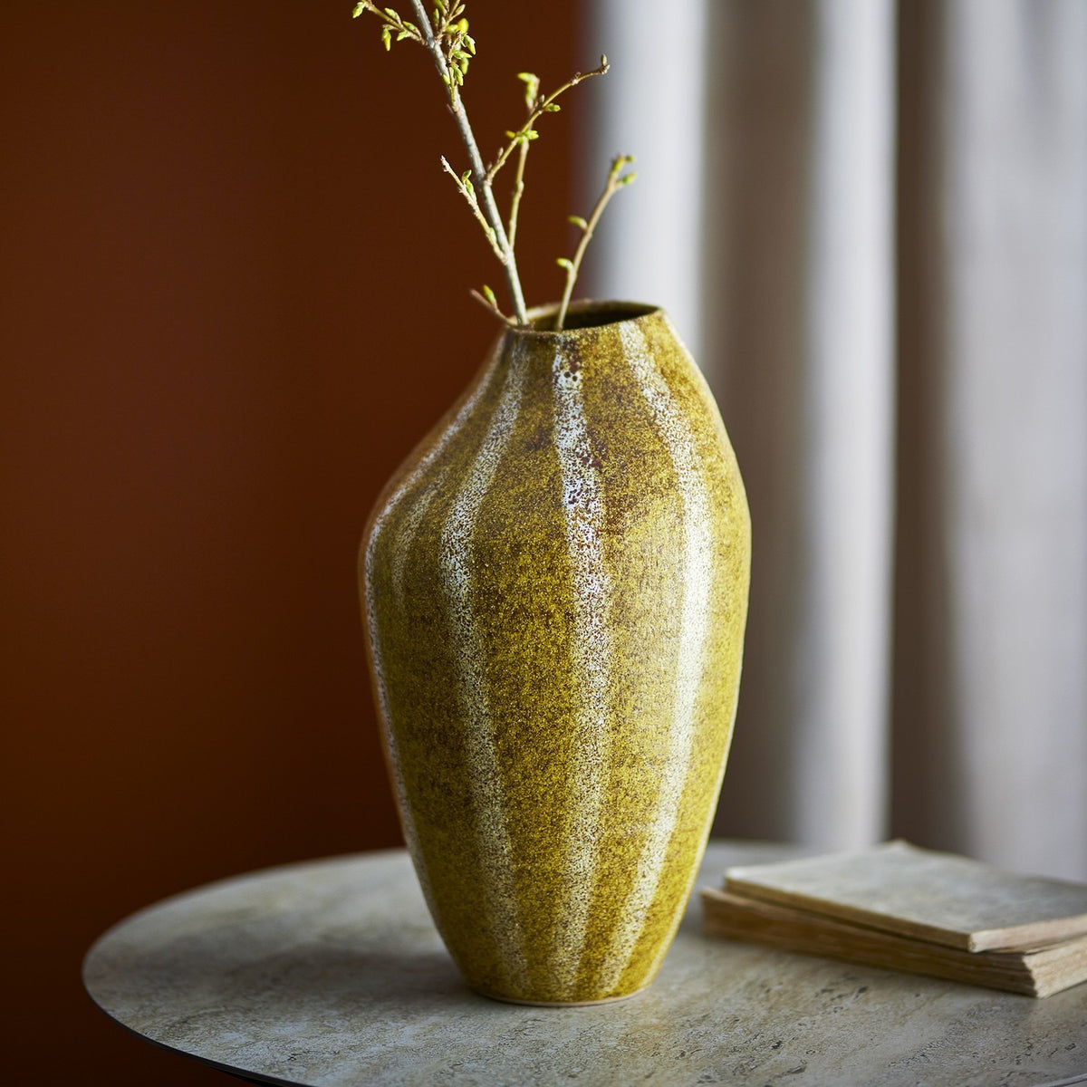 Abella Speckled Stoneware Vase in yellow, 35.5cm tall with a ribbed, asymmetrical silhouette, shown holding budding branches on a stone side table.