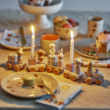 Junaid Cat Birthday Decoration wooden train with animal figures and gift-box candle holders, lit birthday candles, on a festive table set with plates and cups.