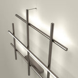 Hilow LED wall light in Brushed Titanium, an open lattice of slim crossing rods with one bar holding a black diffuser for a glowing line, shown against a neutral wall.