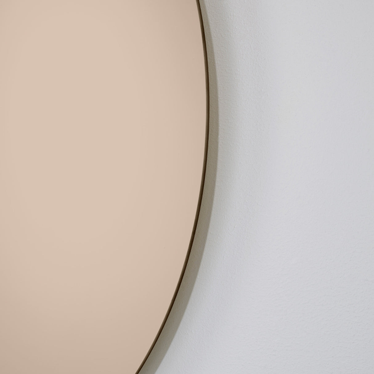 Close-up of the curved bronze tinted edge against a pale wall, the tint deepening towards the rim of the glass.