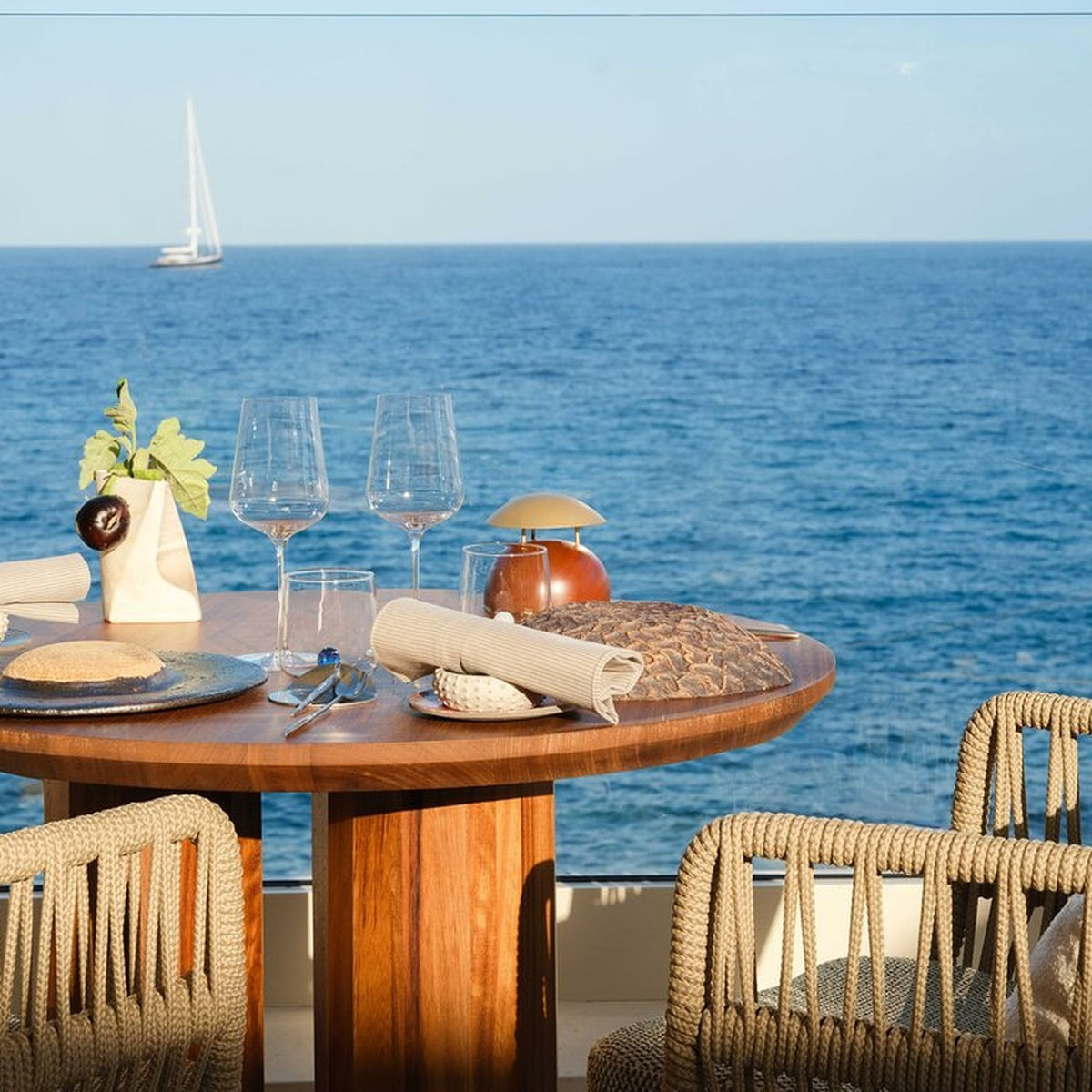 Bell LED Wooden Rechargeable Outdoor Table Lamp IP45 with domed brass-coloured shade on a wood base, shown on a seaside dining table with glassware and sea view.