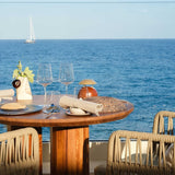 Bell LED Wooden Rechargeable Outdoor Table Lamp IP45 with domed brass-coloured shade on a wood base, shown on a seaside dining table with glassware and sea view.