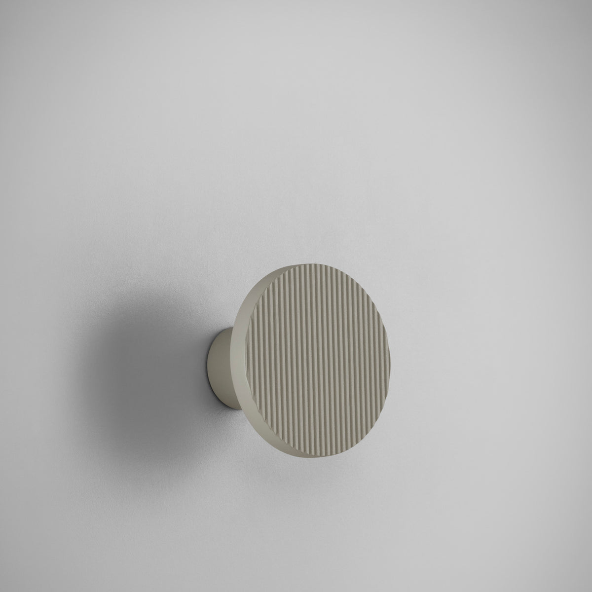 Arid A/01 round aluminium LED wall light with fine vertical fluted disc face in Textured Pebble Grey, mounted on a short cylindrical stem against a plain light background.