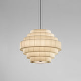 Mos 03 Ribbon Tiered Pendant Light with stacked pleated translucent ribbon rings forming a rounded, dome-like shade in cream, shown lit on a plain grey background.