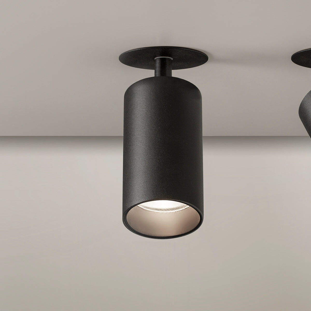 Carl Adjustable Recessed LED Downlight in black, cylindrical head on short stem with round ceiling trim, shown angled with warm white light visible, matt finish.