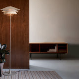 Overlay F Glass Tiered Floor Lamp with layered white glass shades and slim beige stem, shown lit beside a wooden panel in a living room setting.