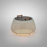 Nans Bag/38/R rechargeable outdoor floor lamp with a low, round open-weave basket shade in beige, a dark lid with two wood handles, illuminated from within, on a plain light background.