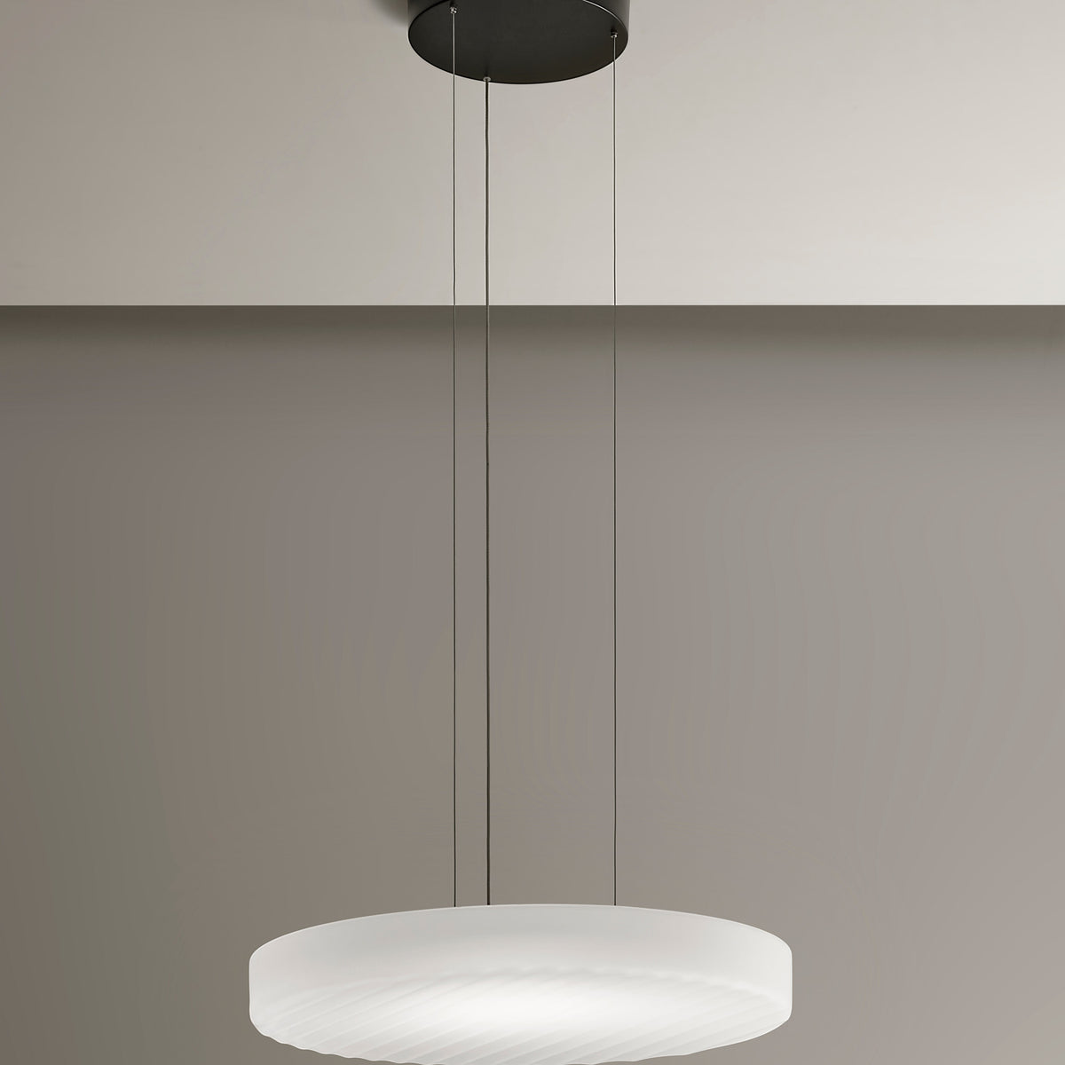 Côte frosted white glass LED pendant light with ribbed underside, suspended from a black ceiling canopy on three thin cables against a neutral wall.