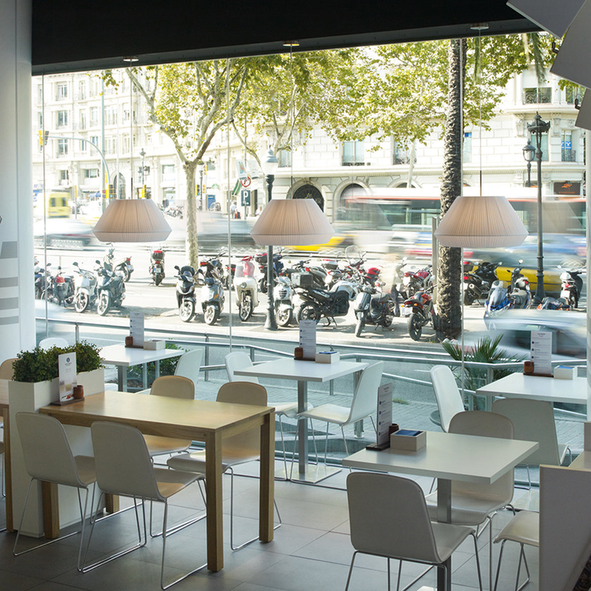 Mei 38 Ribbon Cone Pendant Light in white pleated ribbon shade, cone-tapered, shown above café tables with white chairs beside a street-facing window.