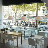 Mei 38 Ribbon Cone Pendant Light in white pleated ribbon shade, cone-tapered, shown above café tables with white chairs beside a street-facing window.