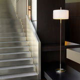 Danona P Fabric Drum Floor Lamp with a white pleated shade on a slim satin nickel stem with dark leather wrap, shown beside a staircase in a modern interior.