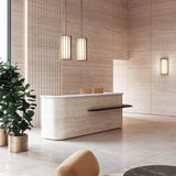 Two Roma Glass LED pendant lights in Brushed Bronze with tall cylindrical slatted shades hang above a travertine reception desk in a modern lobby.