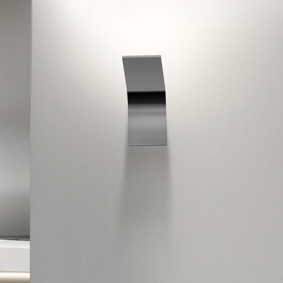 App Aluminium LED Wall Light with a slim curved metal plate in brushed silver finish, mounted on a light grey wall with soft downward glow.