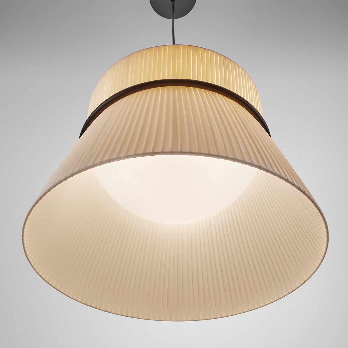 Folie S/60 Ribbon Tiered Pendant Light in cream, pleated fabric shade with straight drum top and tapered lower tier divided by a slim black ring, illuminated against a plain grey background.
