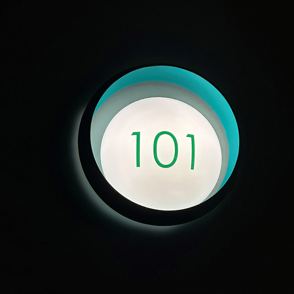 Ring W1 Number Glass Ring Wall Light in black with a teal-lit ring body and illuminated white front disc displaying the green number "101" against a dark background.