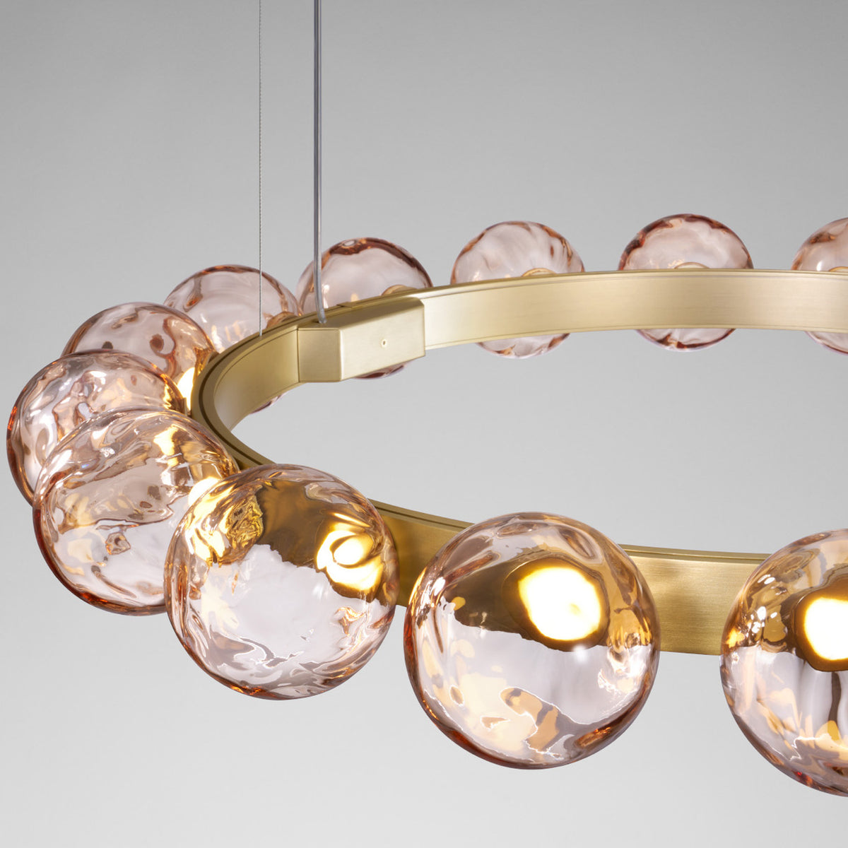 Murané R 25 ring chandelier featuring pink textured glass spheres on a slim Brushed Champagne band, integrated LED lighting, shown close-up against a plain grey background.