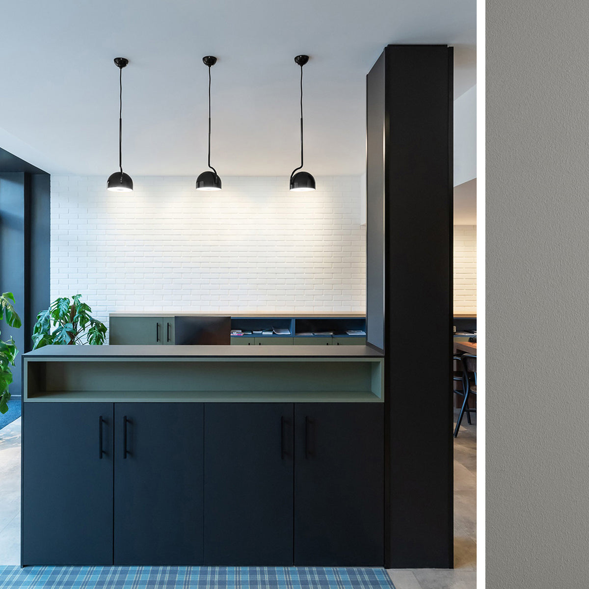 Three Bowee S1 dome LED pendant lights in matte black with slim curved stems, hung above a dark reception counter against a white brick wall.