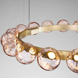 Murané R 18 ring chandelier in brushed champagne, close-up of rippled pink glass spheres glowing warm white, set against a plain grey background.