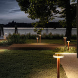 Venexia Glass LED Outdoor Floor Lamp, 70cm wood-effect column with round matt brass and glass head, glowing warm white along a garden path and deck at night.