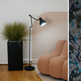 Blux F30 Aluminium Dome Floor Lamp in matte black with jointed arm and round base, shown lit beside a tall grass planter and peach armchair.